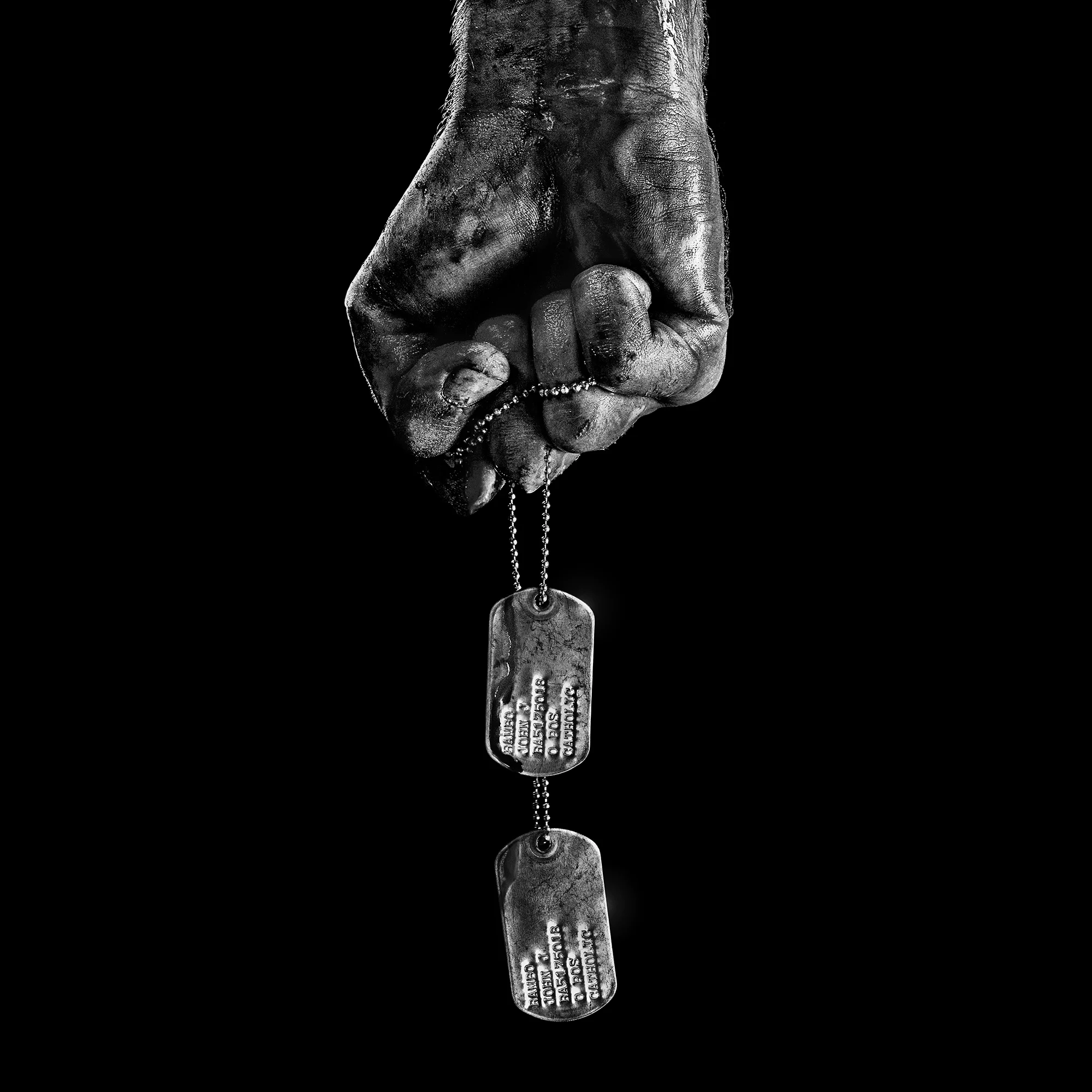 Mão suja segurando dog tags militares representando origem de John Rambo no prequel da franquia